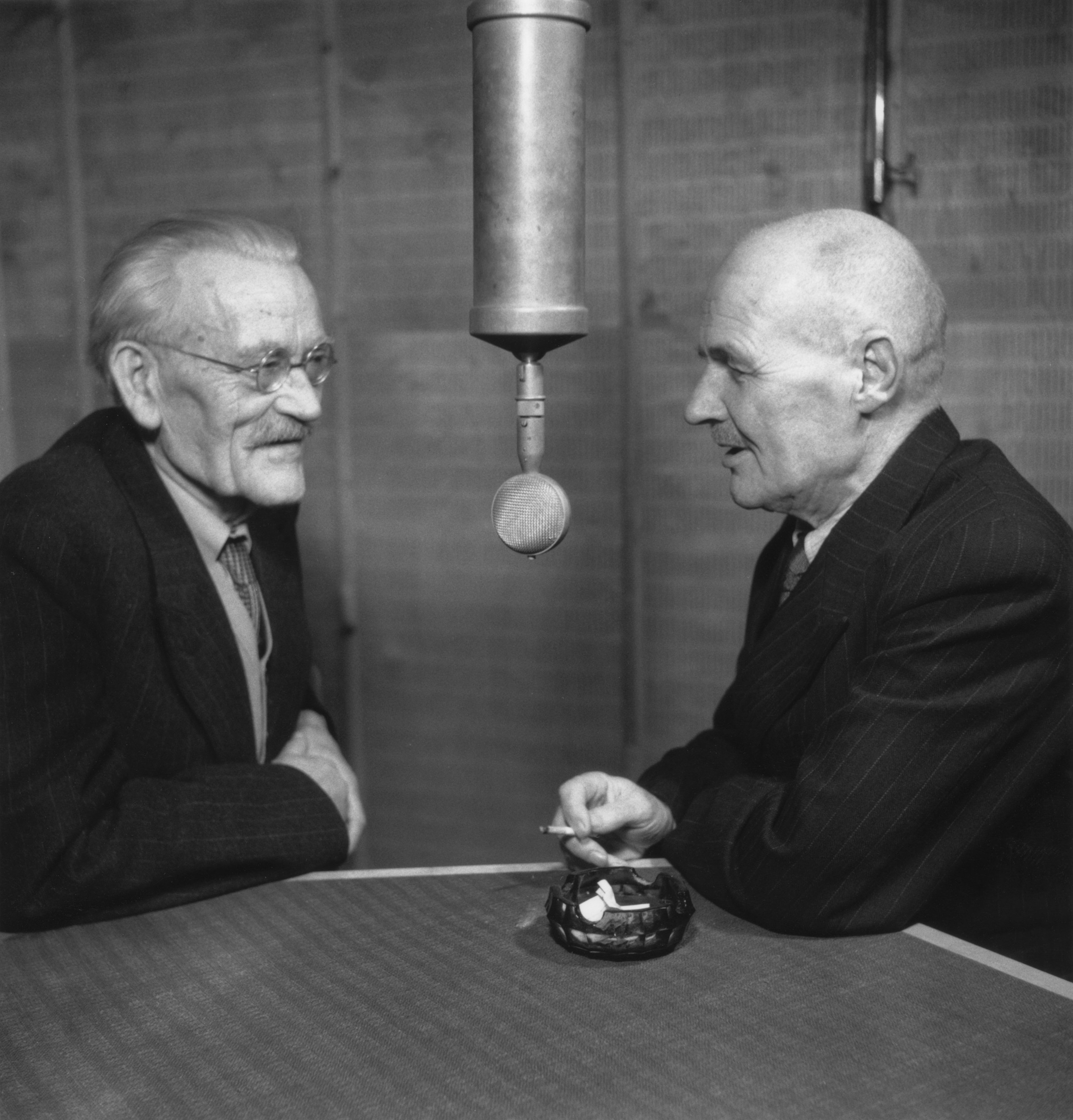 A couple of men sitting at a table next to each other with a microphone between them